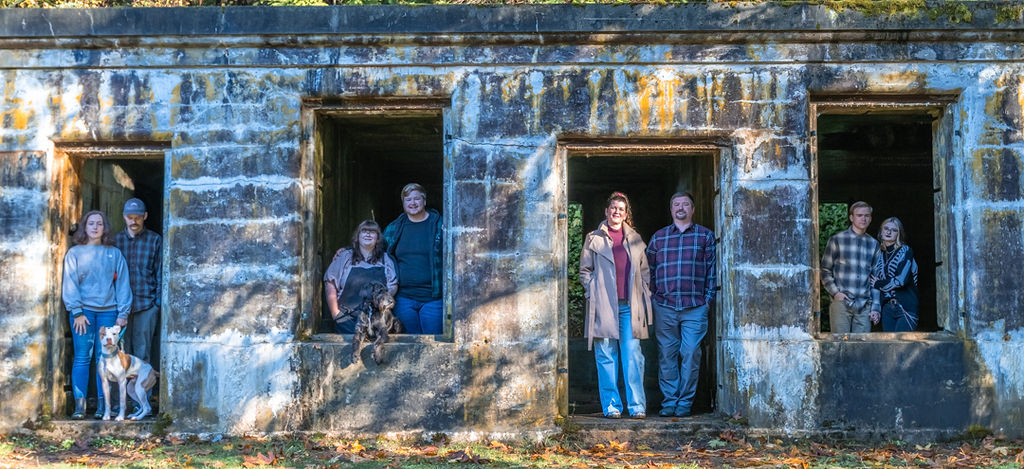 Extended family standing in the window openings of an old stone structure with their dogs in autumn