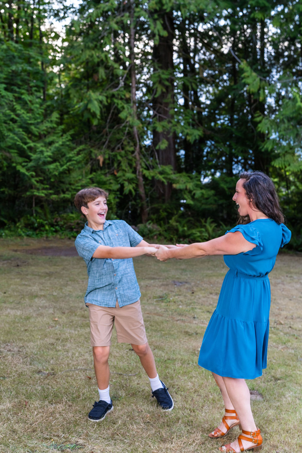 Mother and son laughing and dancing together during an outdoor family photo session in a grassy clearing in Washington