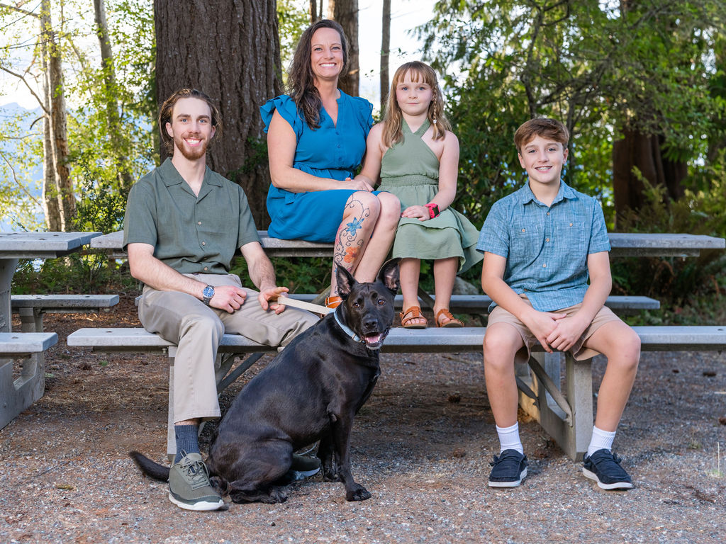 Family of four with their dog seated at a picnic table in the woods