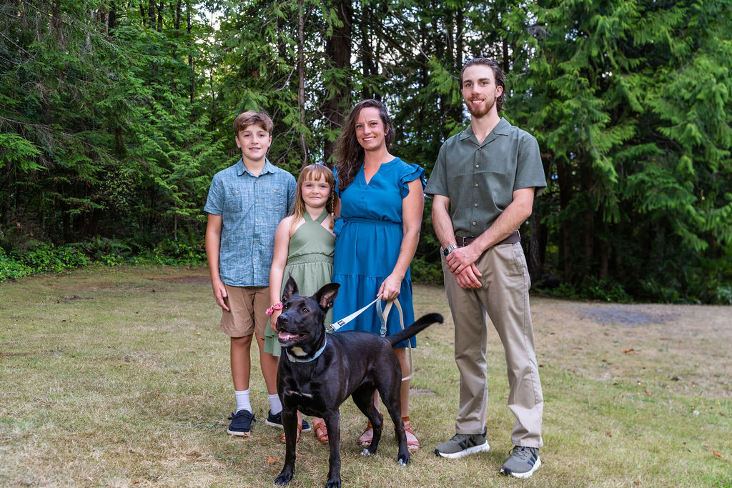 Family of four with their dog standing together in a grassy clearing
