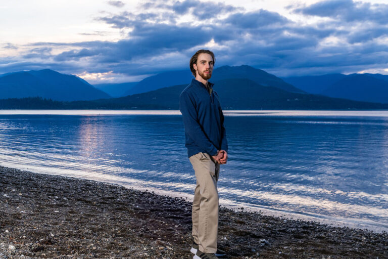 Young man standing on the beach at dusk with the mountains behind him in Kitsap County
