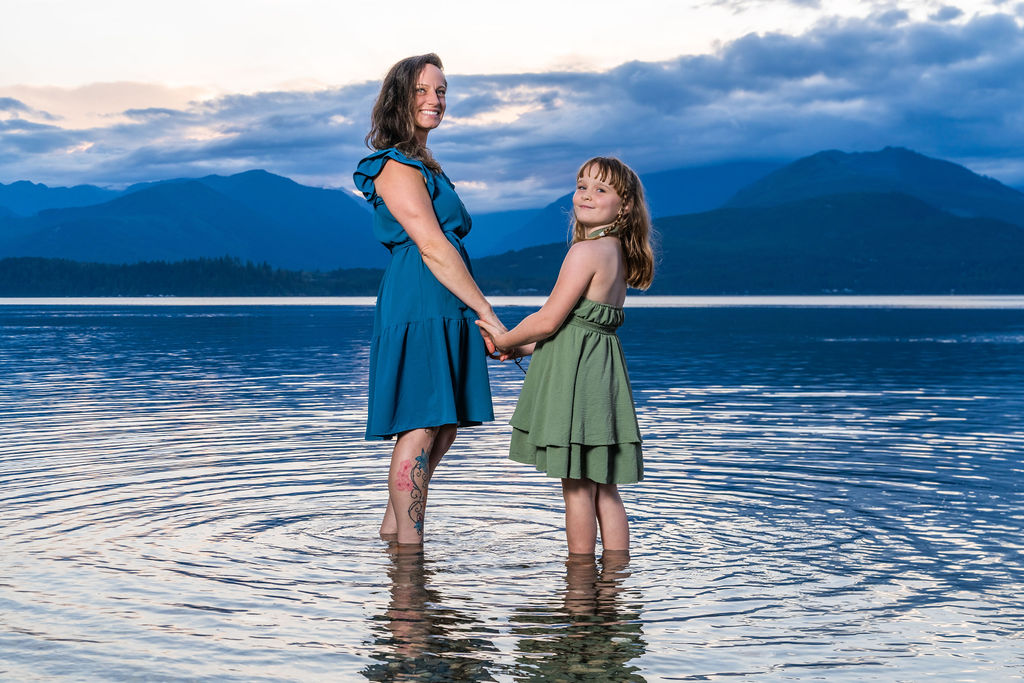 Family photo session with a mother and daughter standing in calm water at dusk in Washington