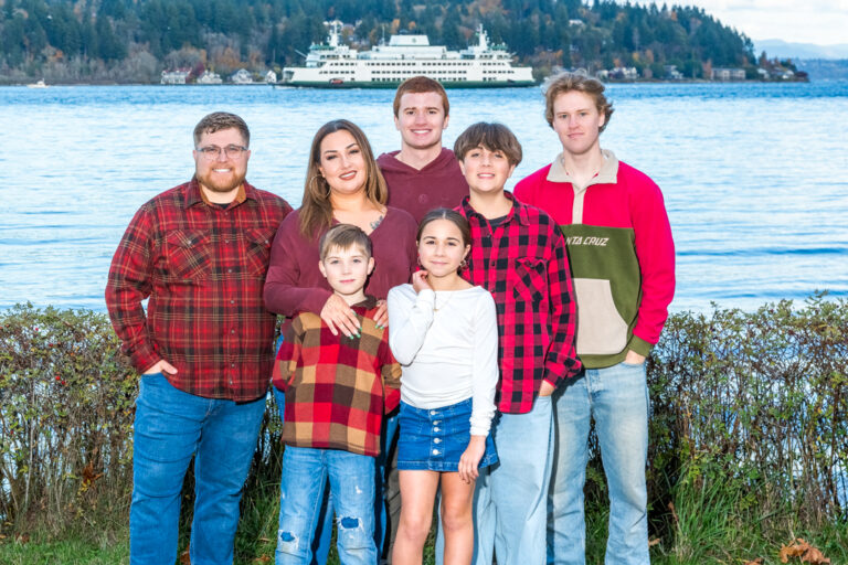 Family portrait beside Puget Sound in Washington with a Washington State Ferry crossing behind them