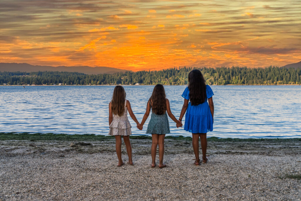 Three young Girls at Manchester State Park holding hand watch a orange sunset.