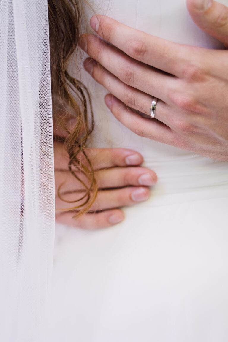 Close detail of the groom's ringed hand resting on the bride's waist