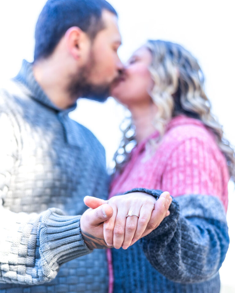 Newly engaged couple kissing with the engagement ring in focus at Manchester State Park in Kitsap County