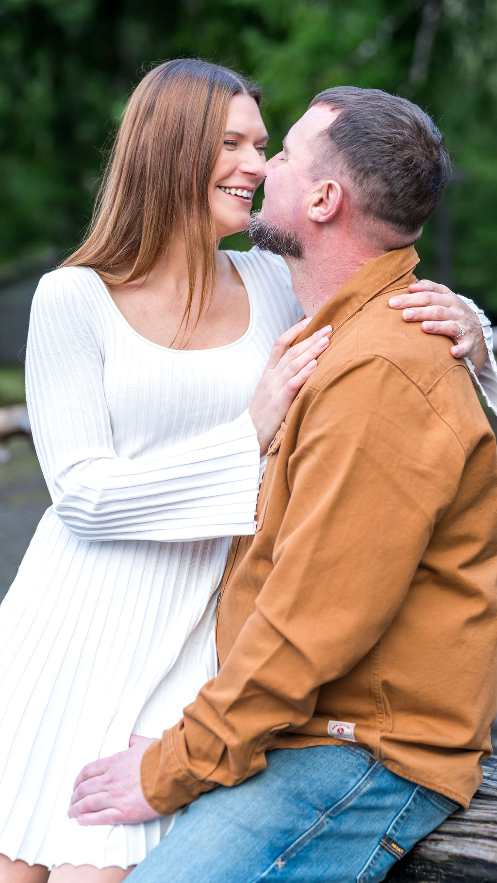Engagement session portrait of a couple laughing together with evergreen trees behind them in the Pacific Northwest