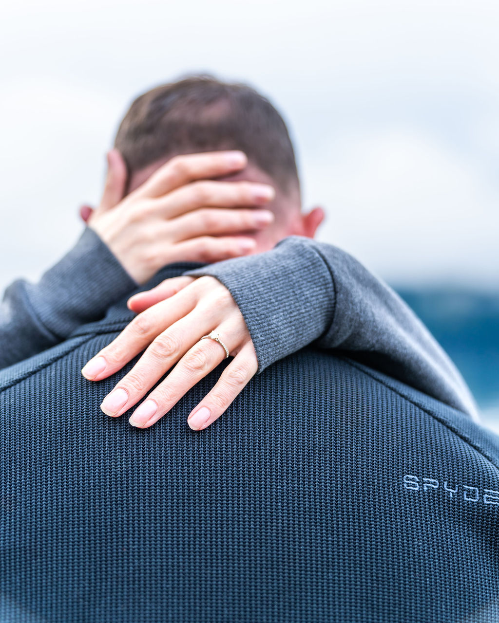 Close-up of an engagement ring as a newly engaged couple embraces during their proposal at Lake Crescent in Olympic National Park.
