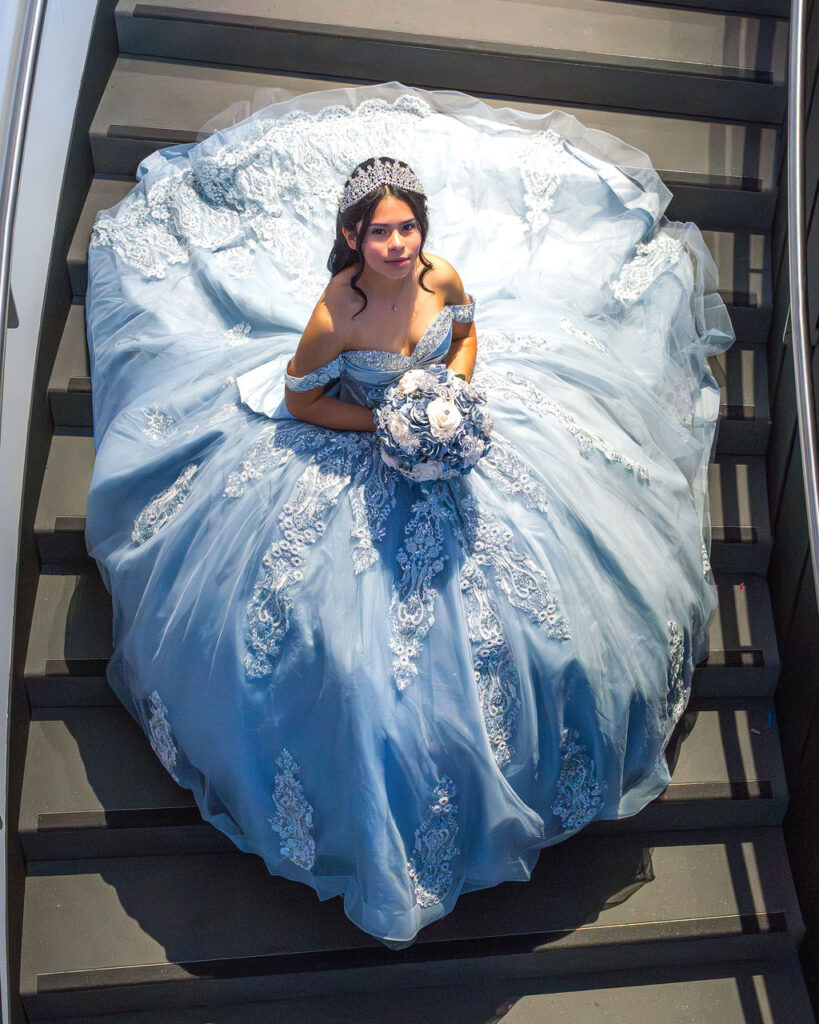 Top-down quinceañera portrait in blue ball gown sitting on staircase