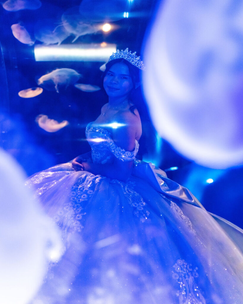 Quinceañera portrait in blue ball gown surrounded by glowing jellyfish at Seattle Aquarium