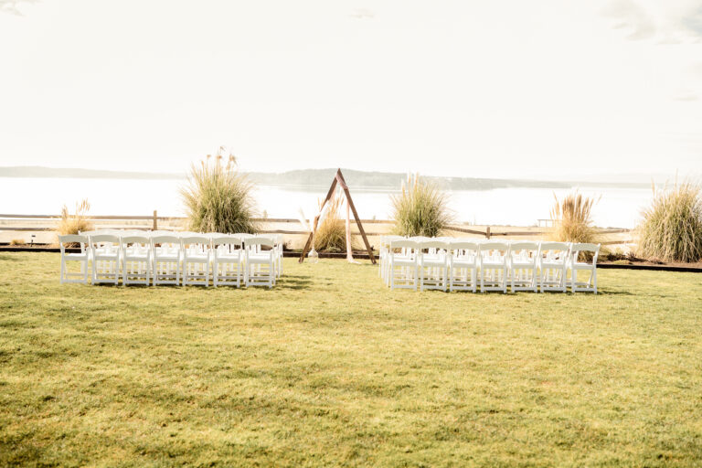 Outdoor waterfront wedding ceremony in Kitsap County with a triangular arch and rows of white chairs overlooking the water