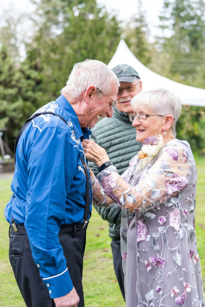 Elderly couple adjusting a boutonniere on a guest’s shirt before a wedding ceremony on Vashon Island, Washington
