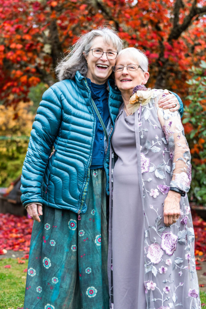 Two wedding guests smiling and posing together in front of colorful autumn foliage at a Vashon Island wedding in Washington
