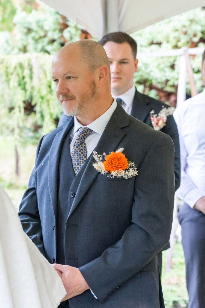 Groom standing under ceremony arch during wedding vows with boutonniere and groomsmen behind him at an outdoor Vashon Island wedding