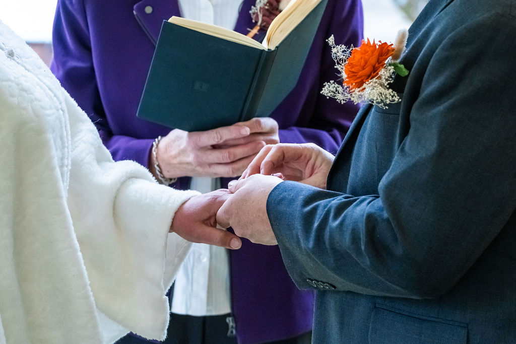 Close-up of bride and groom exchanging wedding rings during an outdoor ceremony with officiant reading from a book on Vashon Island, Washington