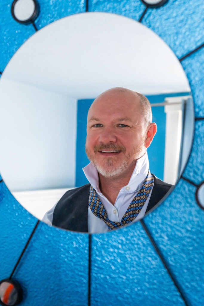 Groom adjusting his collar while getting ready for a Vashon Island wedding reflected in a decorative mirror