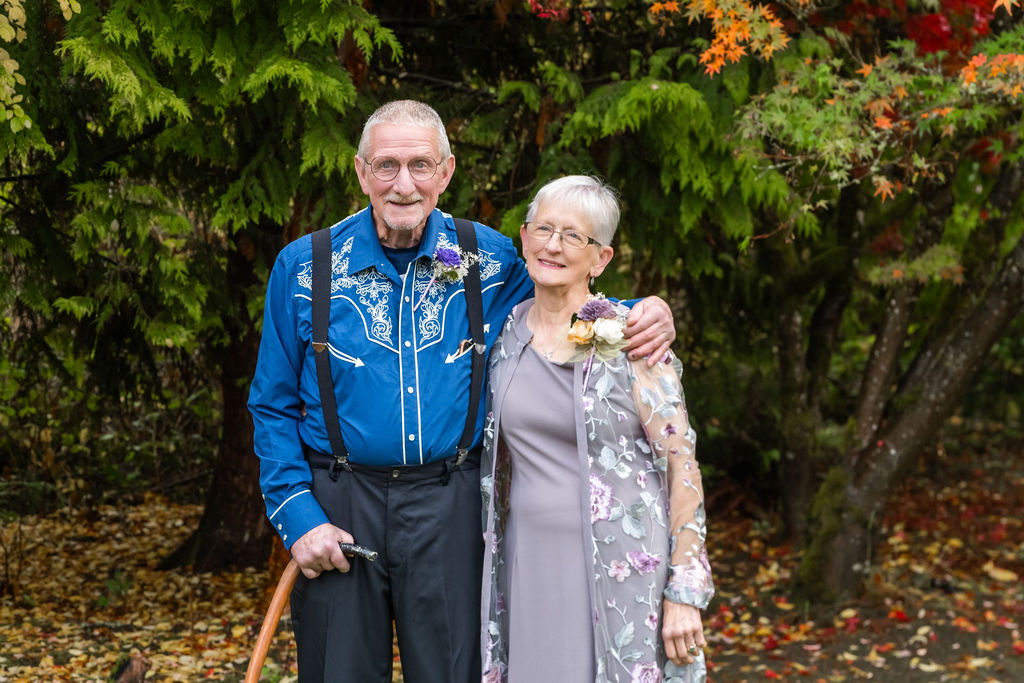 Older couple smiling and posing together in front of colorful fall trees during an outdoor wedding on Vashon Island, Washington