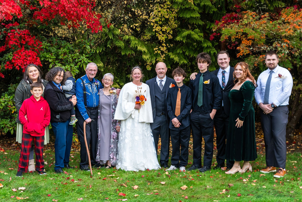Bride and groom standing with extended family members for a large family portrait in front of colorful autumn trees during a Vashon Island wedding