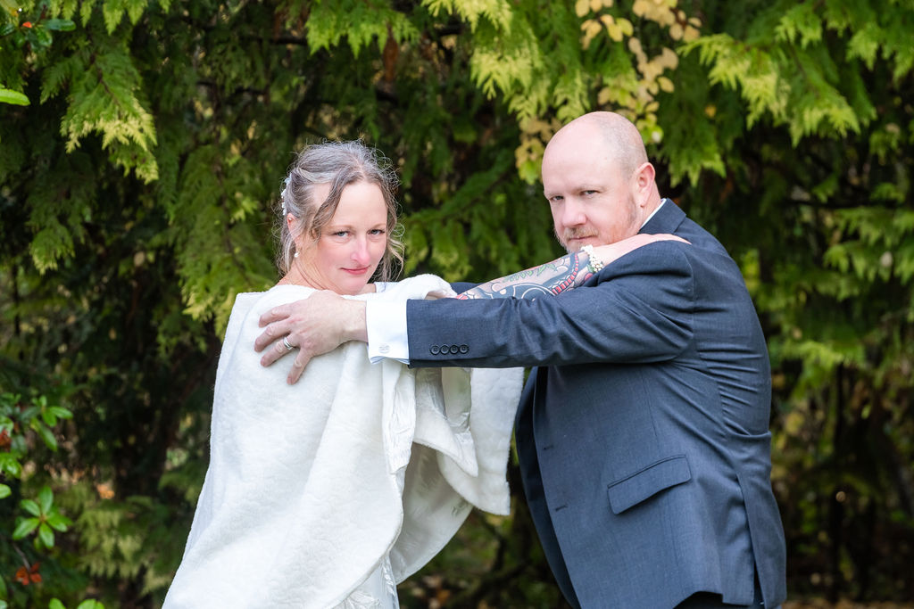 Bride and groom posing playfully with arms crossed while standing together in front of evergreen trees during a Vashon Island wedding portrait session