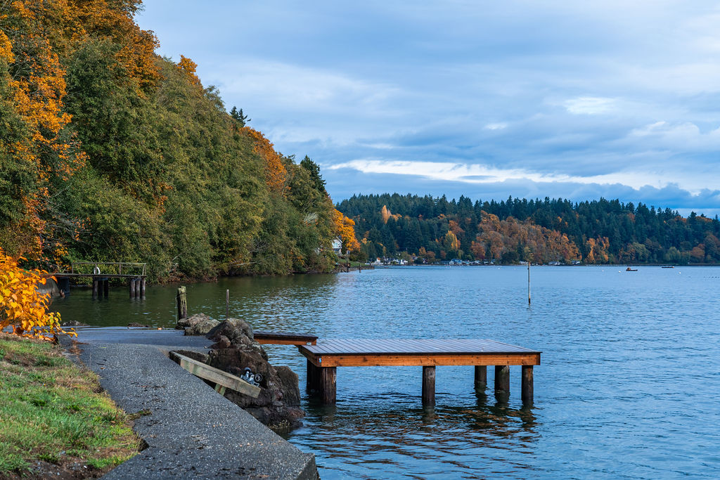 Wooden dock extending into the water with colorful autumn trees along the shoreline on Vashon Island Washington