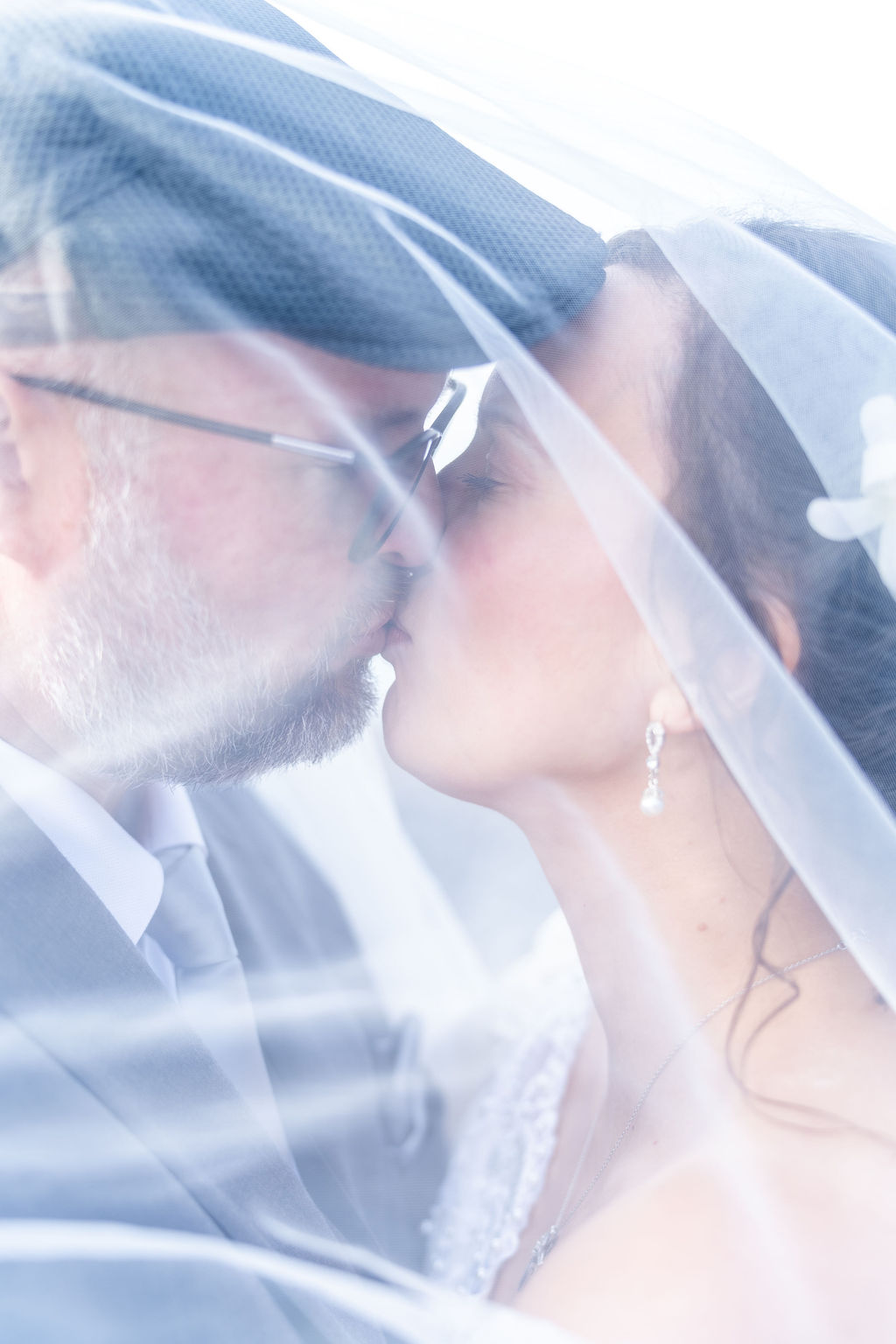 Couple in wedding attire sharing a kiss beneath a veil during portraits in Washington