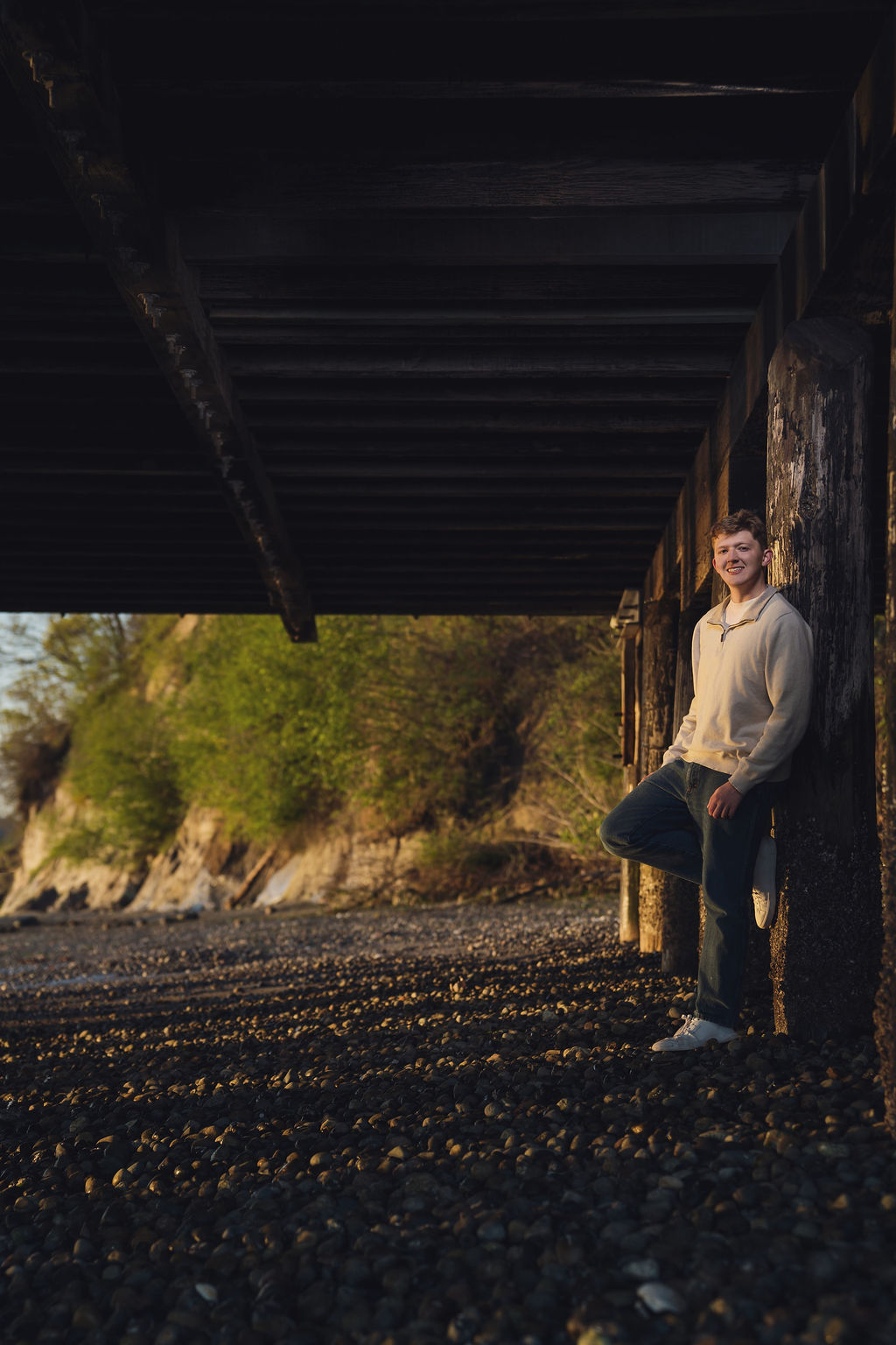 Senior portrait photography at golden hour beneath a pier on a Puget Sound beach in Kitsap County