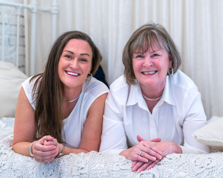 Mother and her adult daughter lying on a crochet blanket smiling at the camera during a holiday studio session in Bremerton