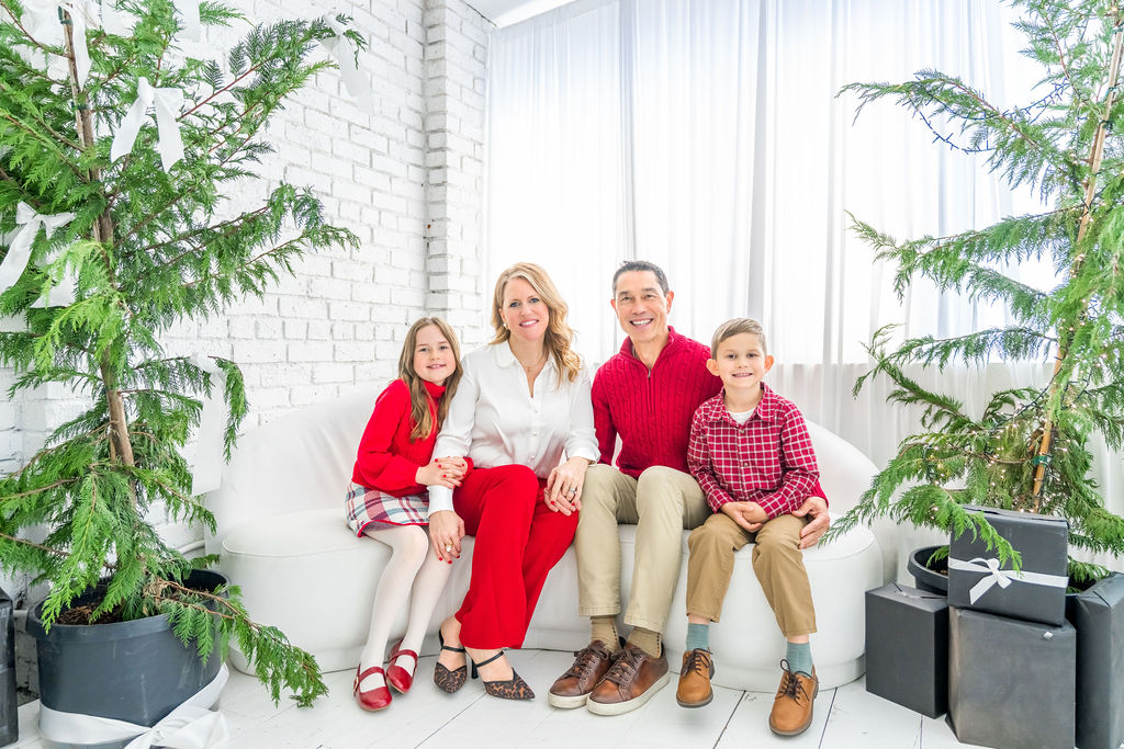Family of four on a white couch surrounded by fresh cedar trees during a holiday studio session in Bremerton