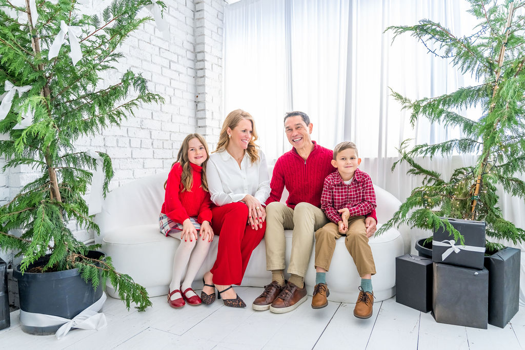 Family of four relaxed together on a white couch surrounded by cedar trees during a holiday studio session in Bremerton