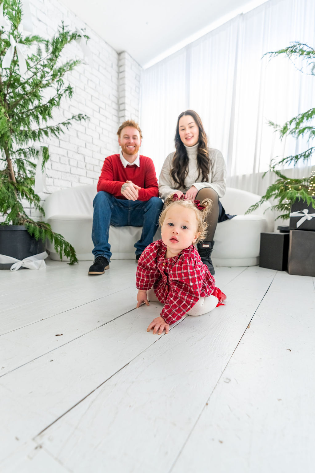 Toddler crawling toward the camera while her parents sit behind her during an indoor family studio session in Washington