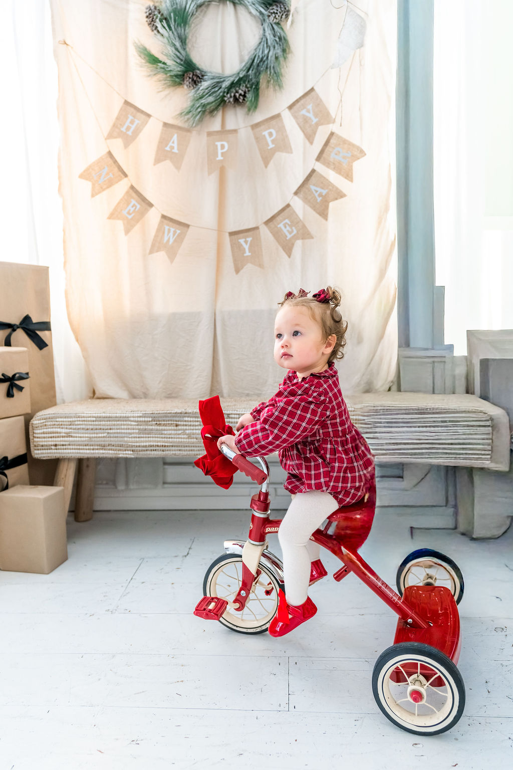 Toddler girl in a red plaid dress on a red tricycle during an indoor family studio session in Washington