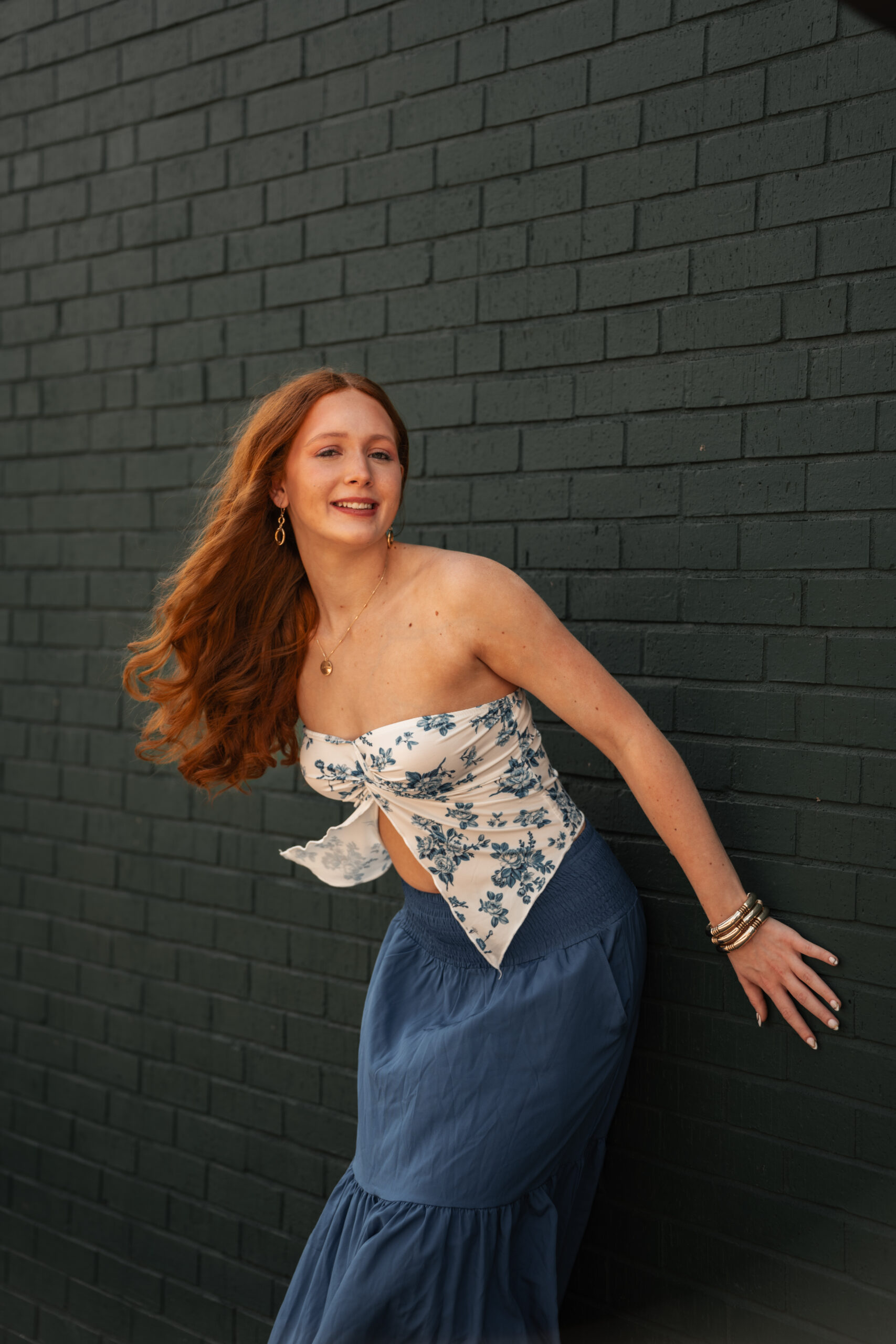 Themed senior portrait of a young woman in a blue costume dress seated on a vintage train under a glittering glass roof