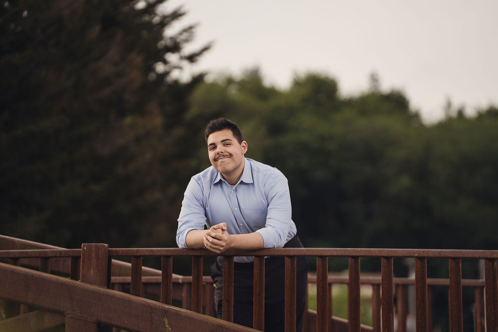 Kitsap County senior photographer portrait of a high school senior in a blue dress shirt leaning on a wooden bridge railing