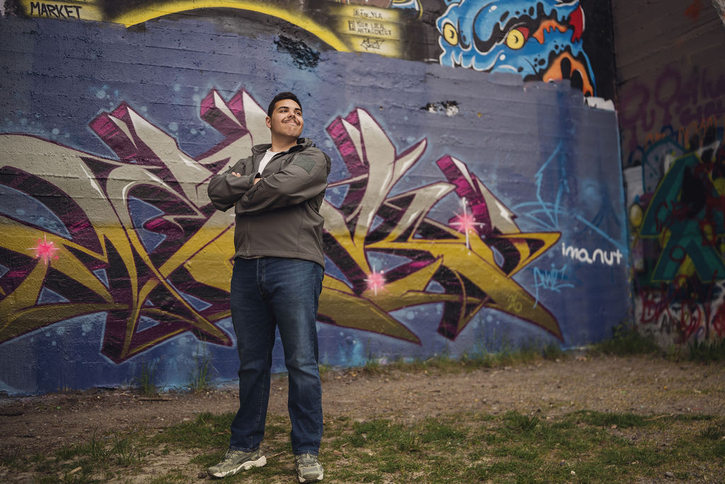 High school senior standing with arms crossed in front of a bold graffiti mural