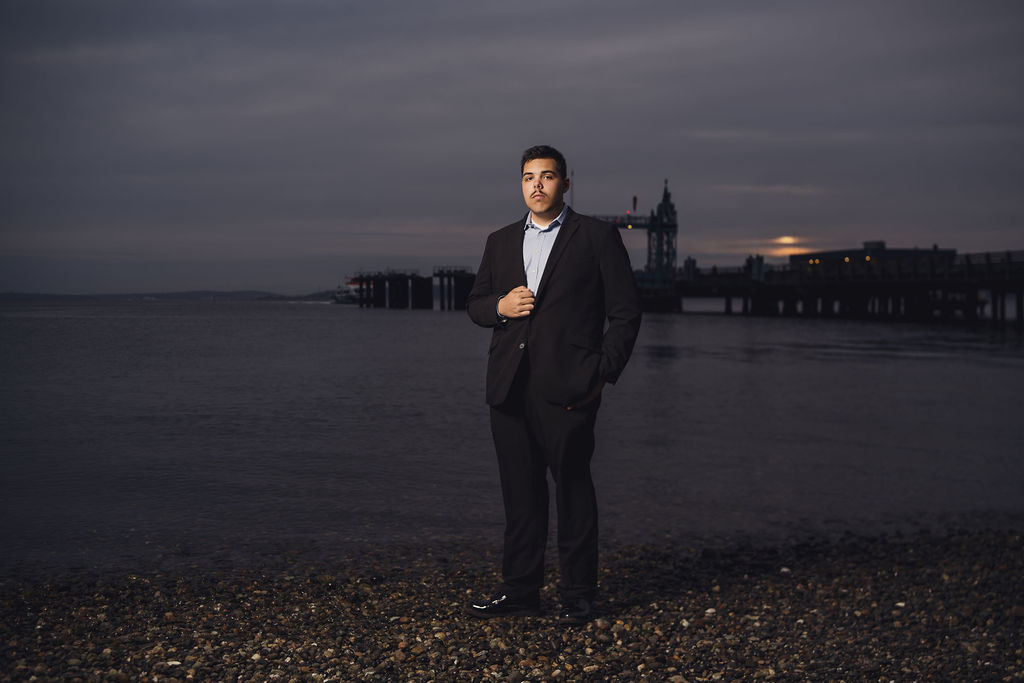 Kitsap County senior photographer portrait of a young man in a suit on a pebble beach at dusk with a pier behind