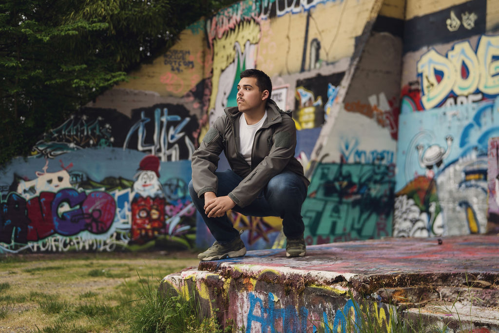 High school senior crouched on a concrete slab in front of a colorful graffiti wall