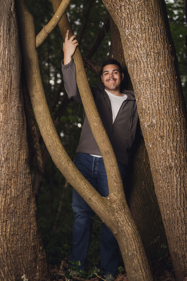 High school senior smiling among curving tree trunks in a forest during a senior portrait session