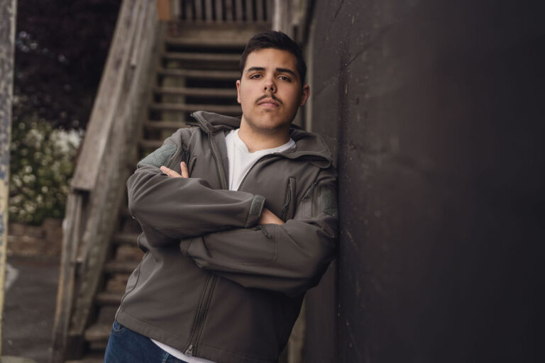 Relaxed senior portrait of a senior in a casual jacket leaning against a wall, an everyday personal look