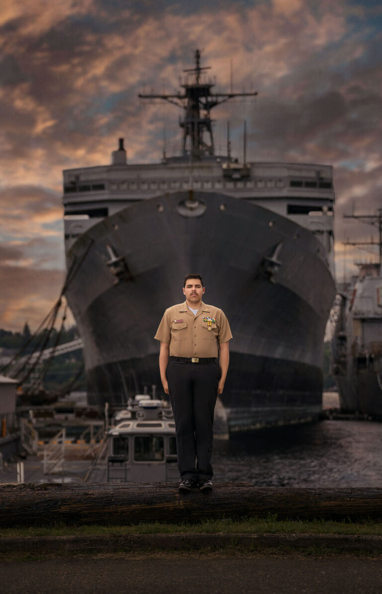 High school senior guy in a Navy dress uniform in front of a Navy ship at sunset