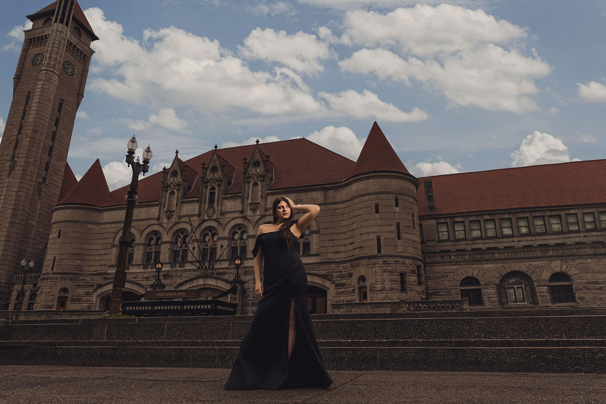 High fashion senior portrait of a young woman in a black gown in front of a grand historic stone building with a clock tower