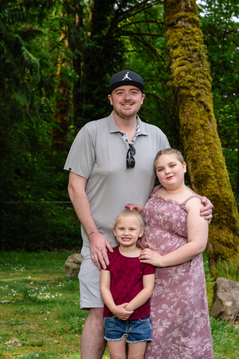 Father with his two daughters posing by a mossy tree at a green Kitsap County park