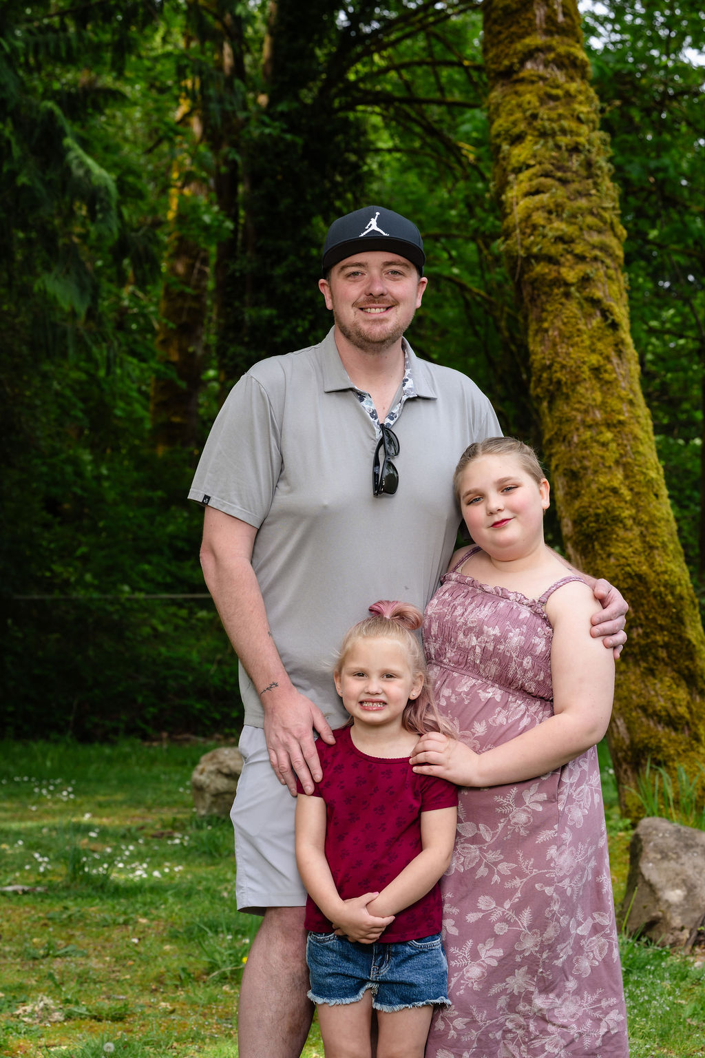 Father with his two daughters posing by a mossy tree at a green Kitsap County park