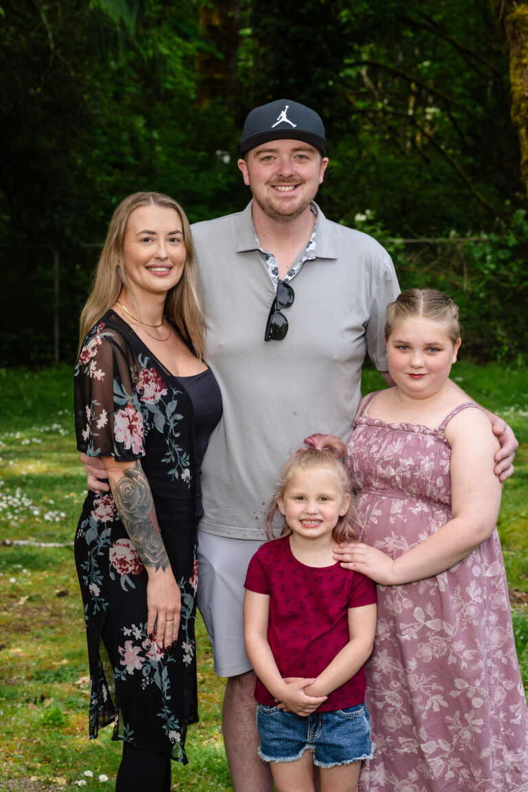 Family of four with two daughters posing together by the trees at a Kitsap County park
