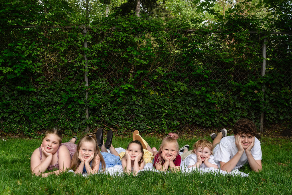 Six children lying in a row in the grass with their chins on their hands at a Kitsap County park