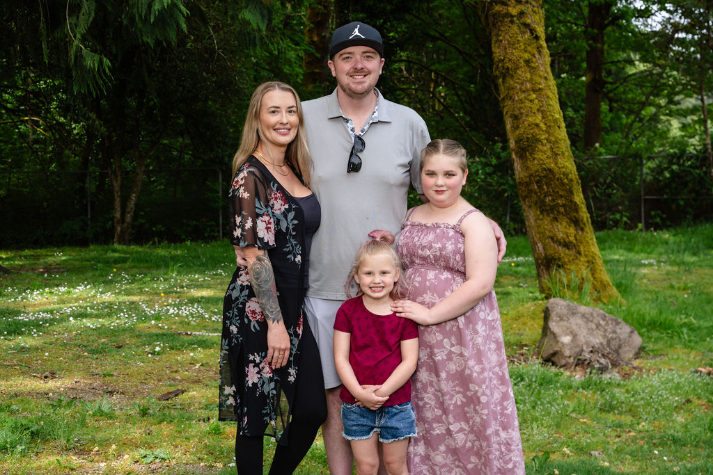 Family of four with two daughters posing together by a mossy tree at a green Kitsap County park