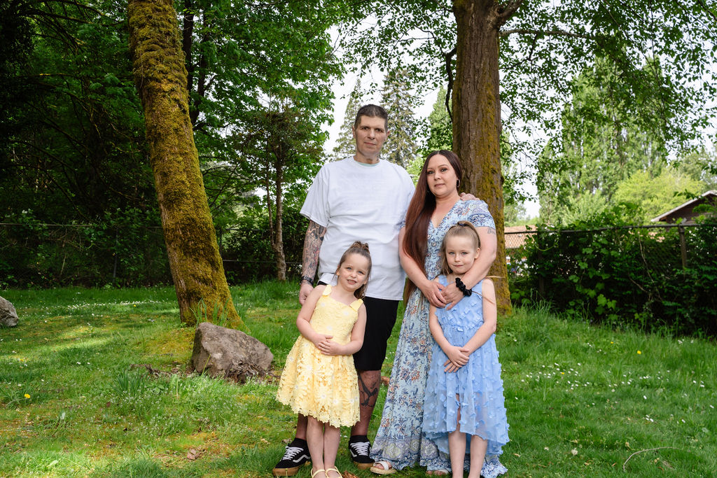 Family of four with two daughters in spring dresses posing among the trees at a Kitsap County park
