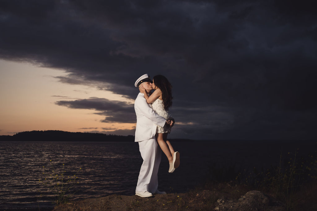 Navy officer lifting his fiancee for a sunset kiss on the bluff at Chambers Bay near Tacoma