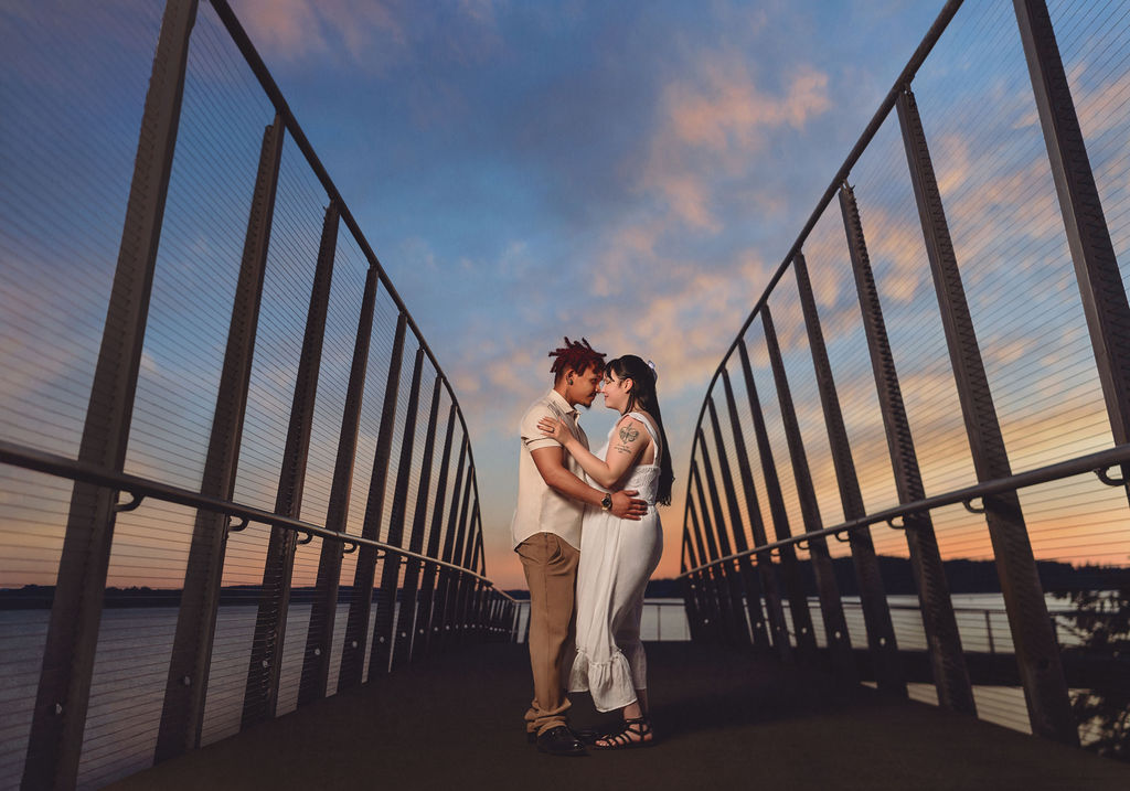 Engaged couple forehead to forehead on the boardwalk pier under a dramatic pastel sky at Chambers Bay near Tacoma