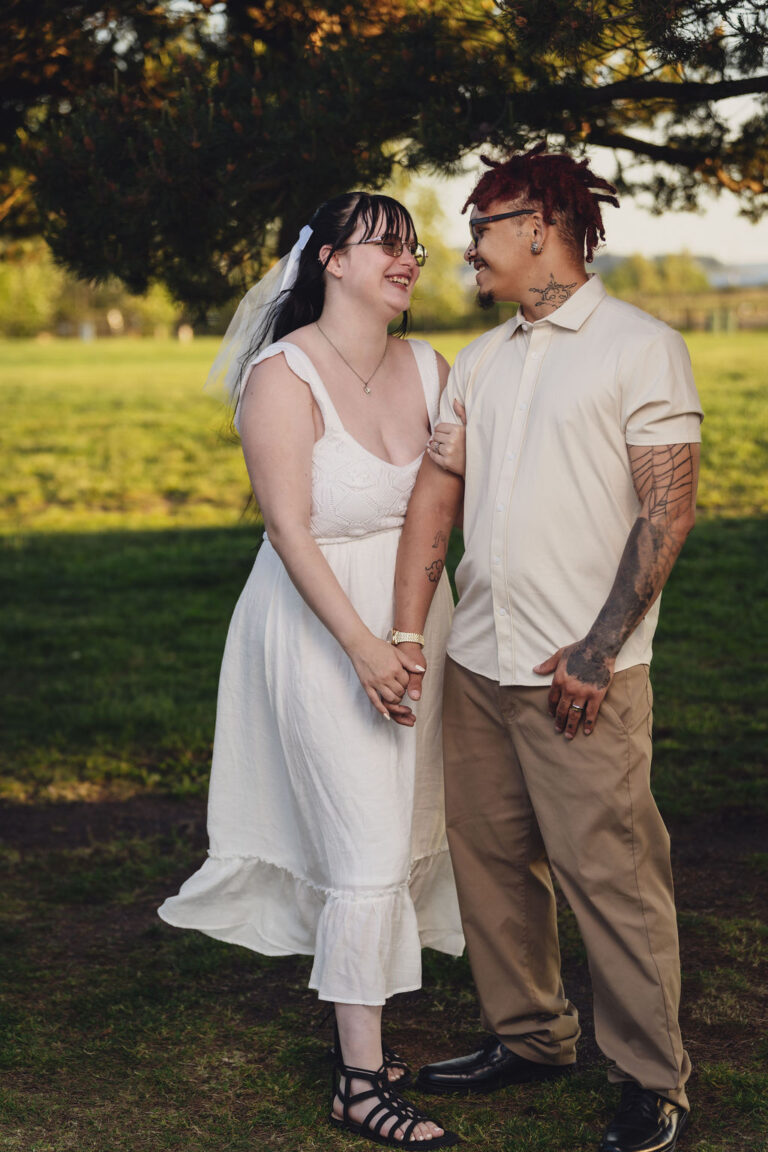 Engaged couple laughing together while holding hands in a park meadow at Chambers Bay near Tacoma. what to do with hands engagement photos