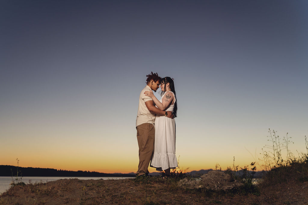 Engaged couple embracing forehead to forehead on a bluff at twilight at Chambers Bay near Tacoma